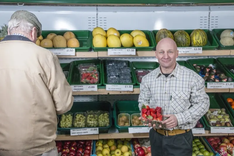 Primeur souriant servant un client devant ses étals de fruits et légumes