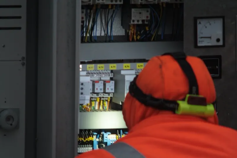 Électricien en tenue haute visibilité, lampe frontale sur la tête, travaillant sur une armoire électrique