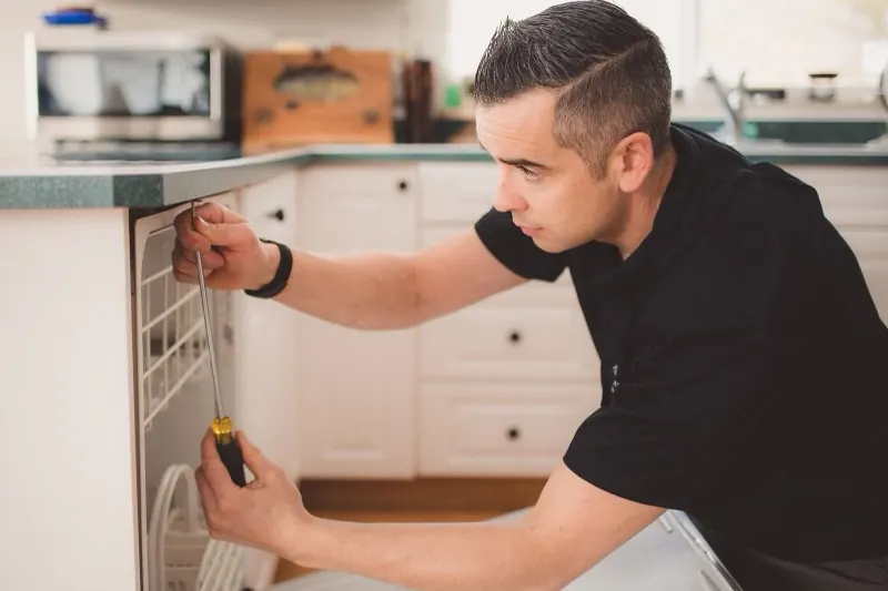 Artisan plombier installant un lave-vaisselle dans une cuisine lumineuse